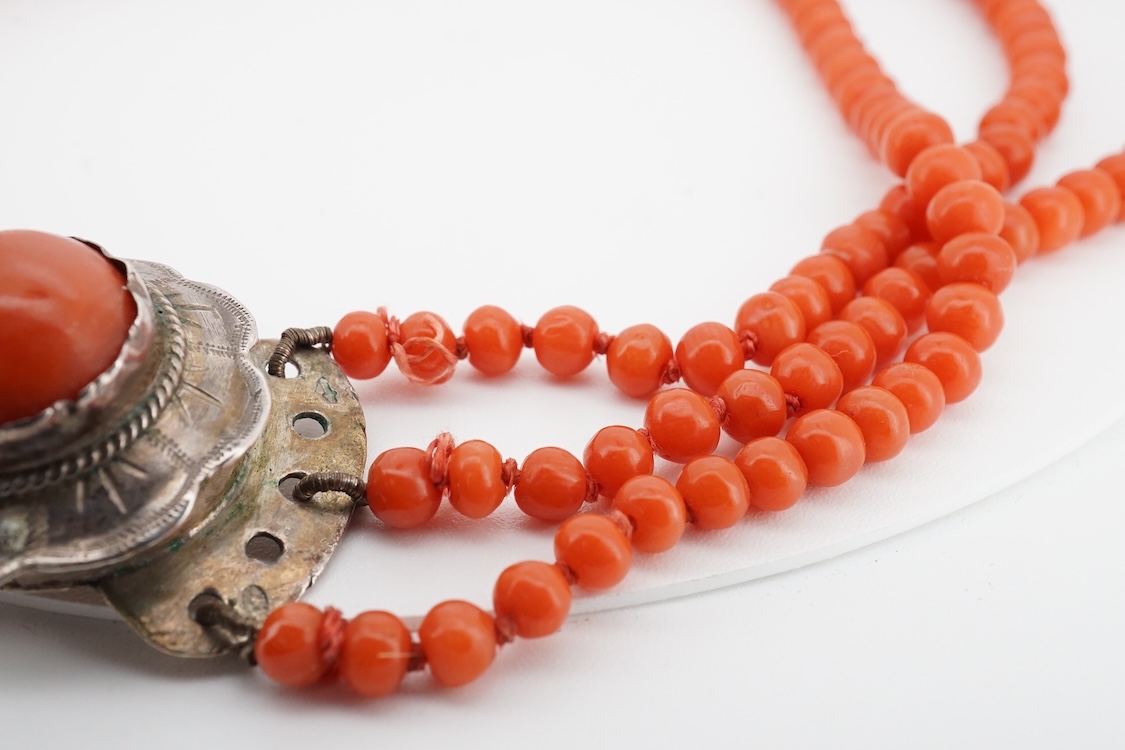 A triple strand graduated coral bead choker necklace, with a cabochon coral set white metal clasp, 38cm.